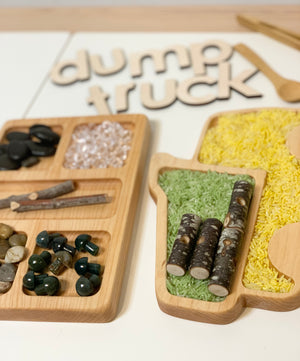 Wooden dump truck shaped sensory tray with compartments filled with colored rice and small natural materials on white surface