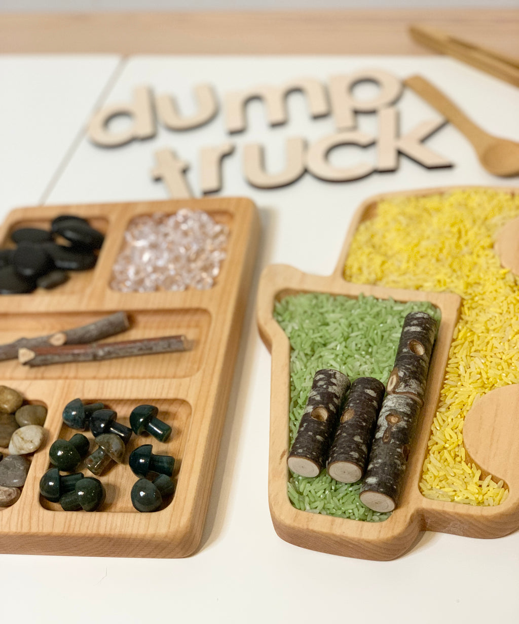 Wooden dump truck shaped sensory tray with compartments filled with colored rice and small natural materials on white surface