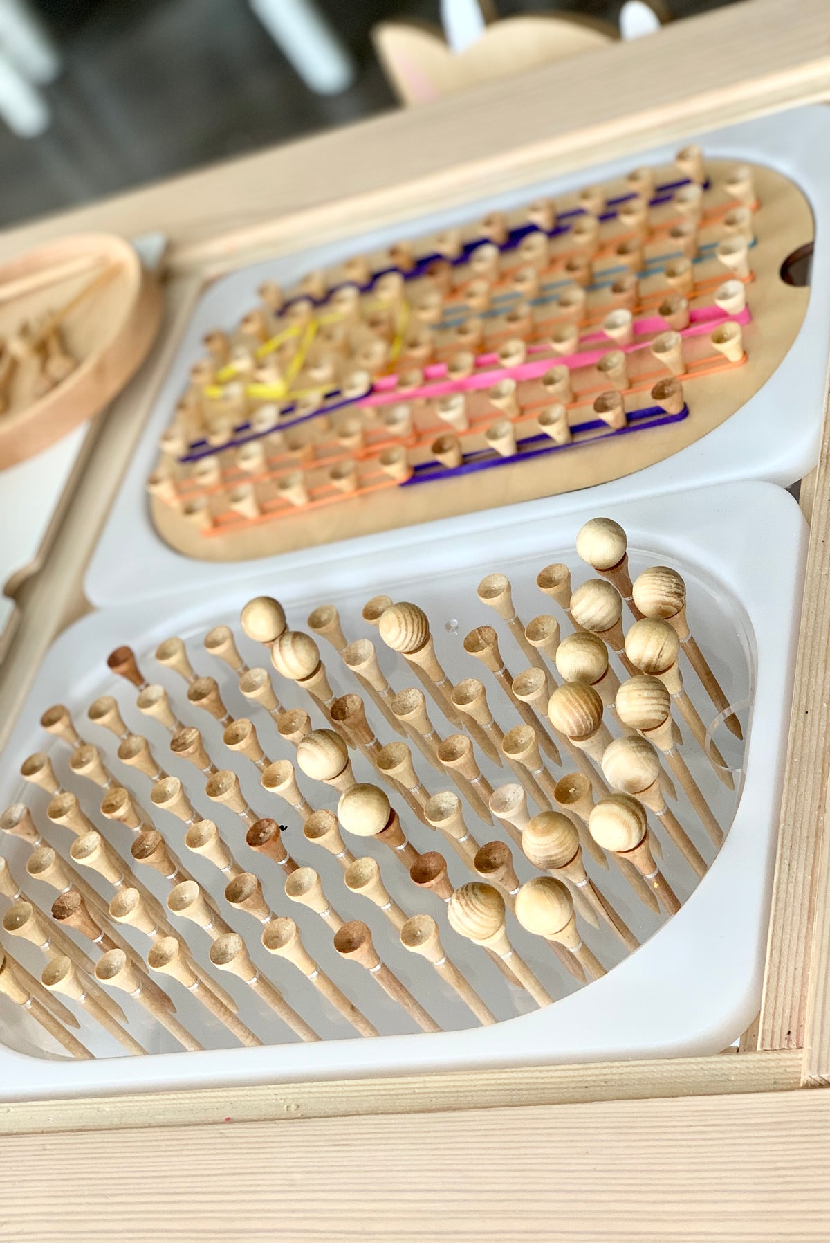 Wooden peg board insert with round-tipped pegs arranged on white tray fitted into Flisat table wooden frame