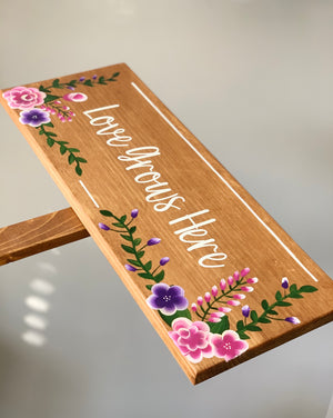 Large custom wooden garden sign with white cursive lettering and pink and purple floral illustrations on natural wood background