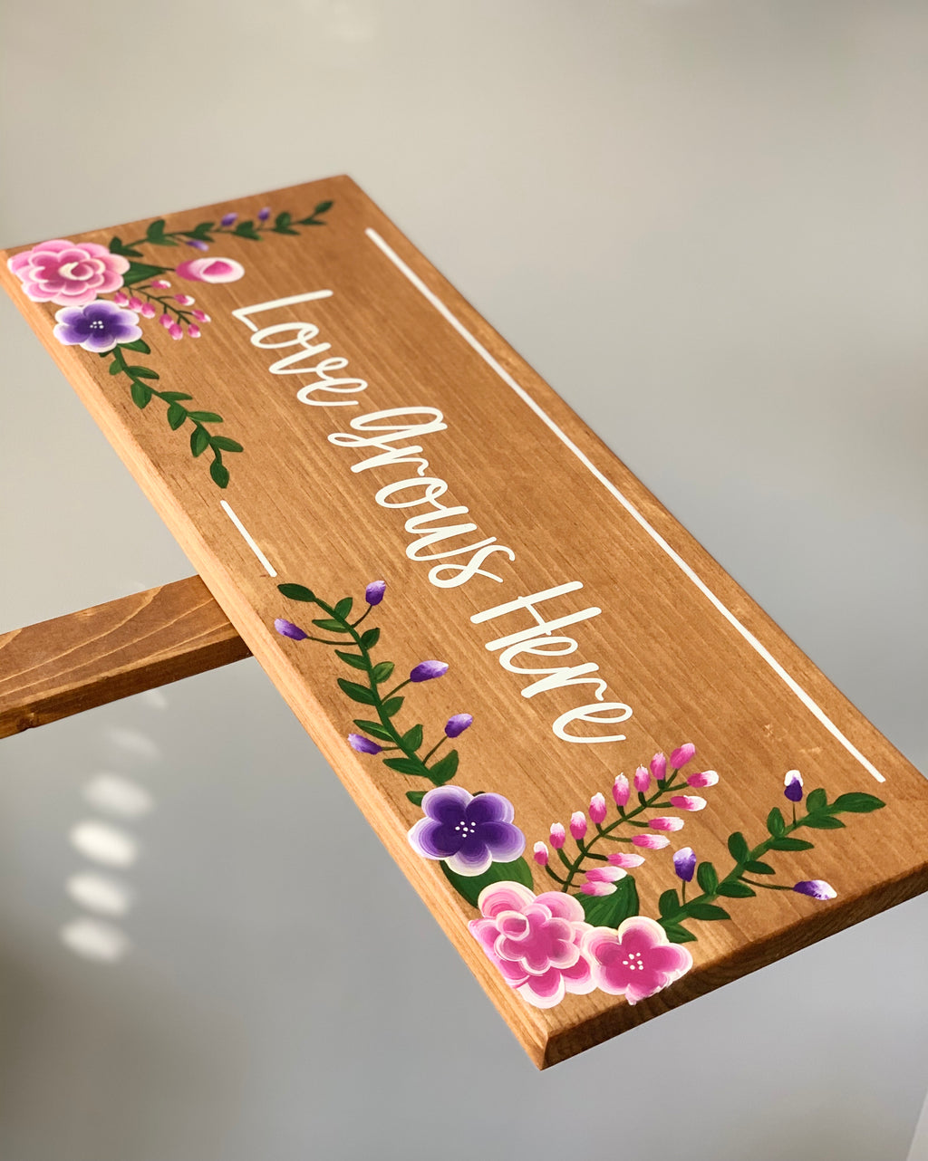 Large custom wooden garden sign with white cursive lettering and pink and purple floral illustrations on natural wood background