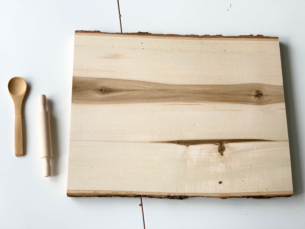 Live edge wooden tray with natural bark edges and wood grain, next to small wooden spoon and rolling pin on white surface