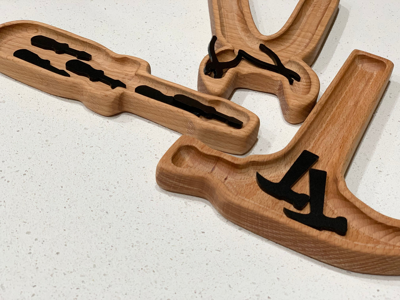 Set of three wooden trays with black acrylic tool-shaped inserts for sensory play on white surface