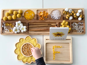 Wooden sensory tray with yellow and clear tactile objects and sunflower-shaped plate with yellow rice and corn kernels