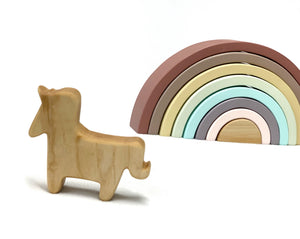 Small natural wooden unicorn toy figurine standing next to pastel-colored wooden rainbow stacking toy on white background