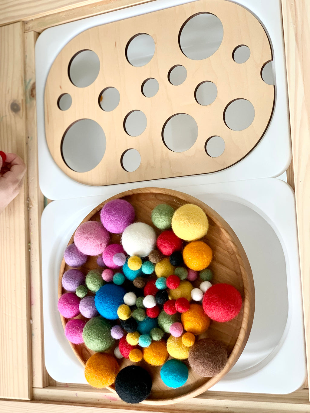 Circle sorter wooden table top insert with various-sized holes and colorful felt balls on wooden surface