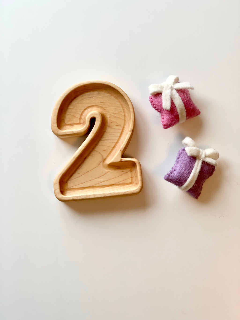 Natural wooden number plate shaped as number 2 with two small wrapped felt sensory toys on white background