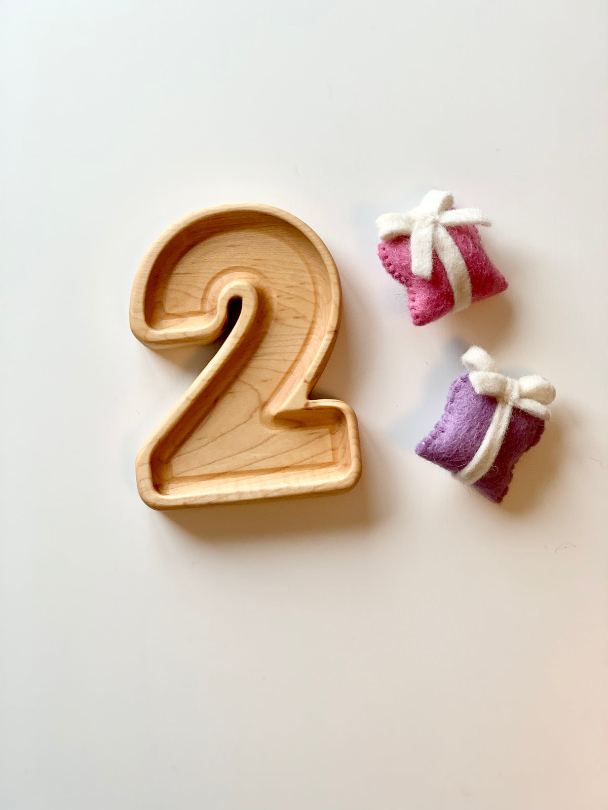 Natural wooden number plate shaped as number 2 with two small wrapped felt sensory toys on white background