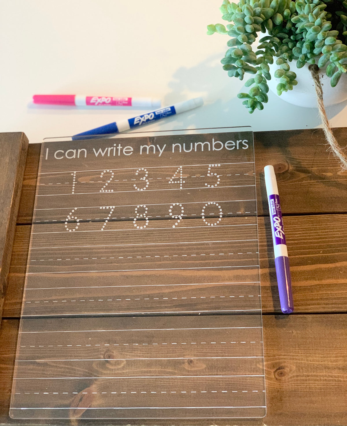 Clear acrylic dry erase board engraved with numbers 1 to 10 for tracing and writing practice with three dry erase markers on wood background