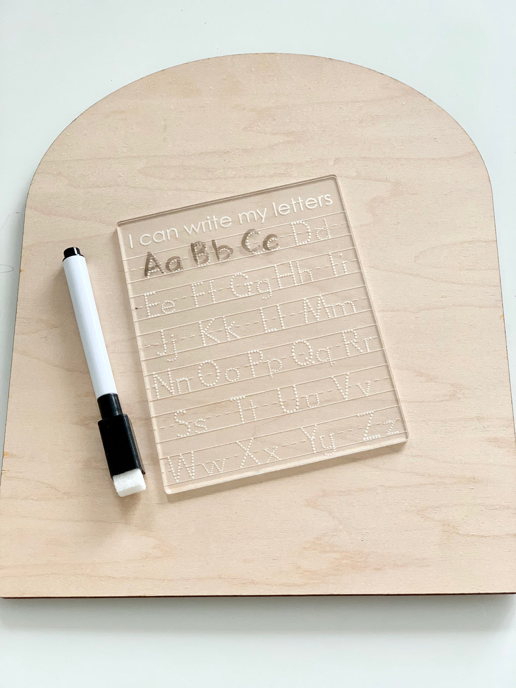 Mini acrylic dry erase tracing board with uppercase and lowercase letters and black dry erase marker on wooden surface