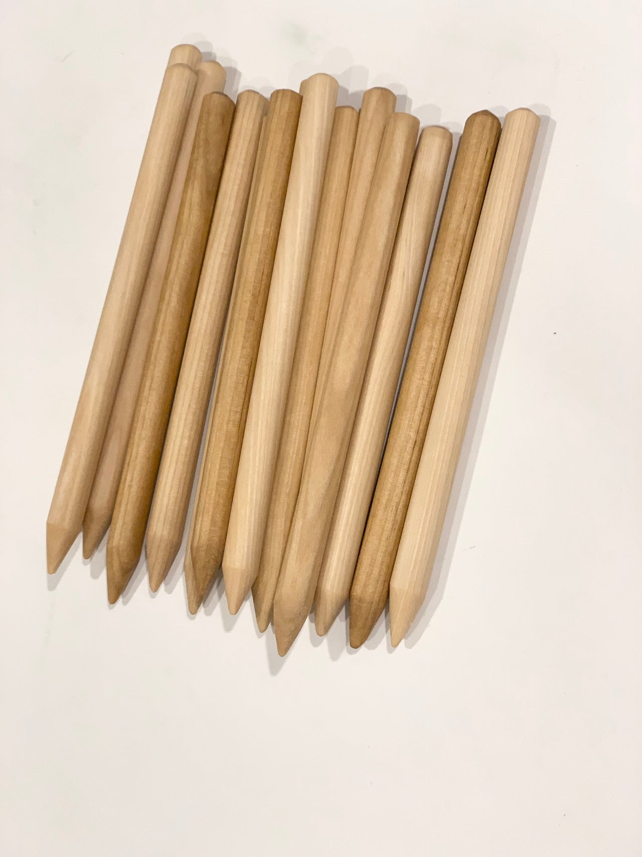 Set of natural wooden styluses with rounded ends and pointed tips arranged in rows on white background