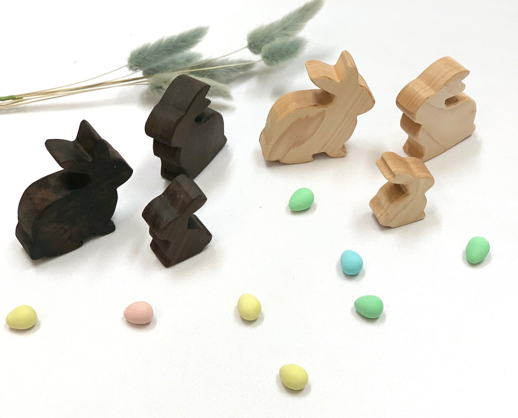 Set of dark and light natural wooden toy bunnies arranged with pastel colored eggs and dried grass on white surface
