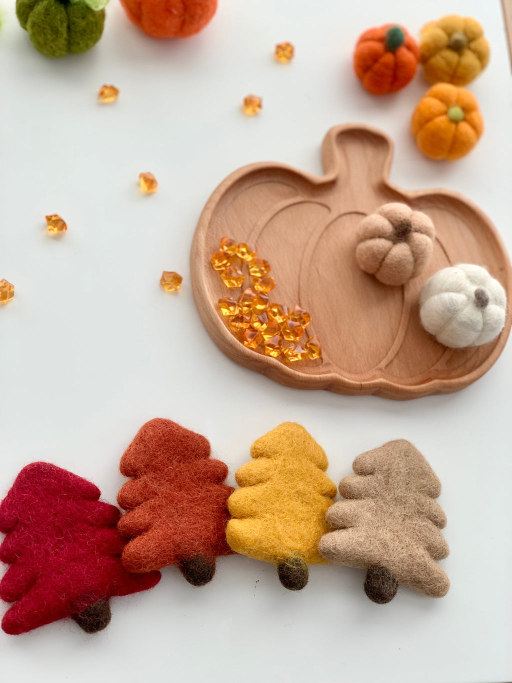 Natural wooden pumpkin-shaped plate with orange gems and felt pumpkin and tree sensory play pieces on white background