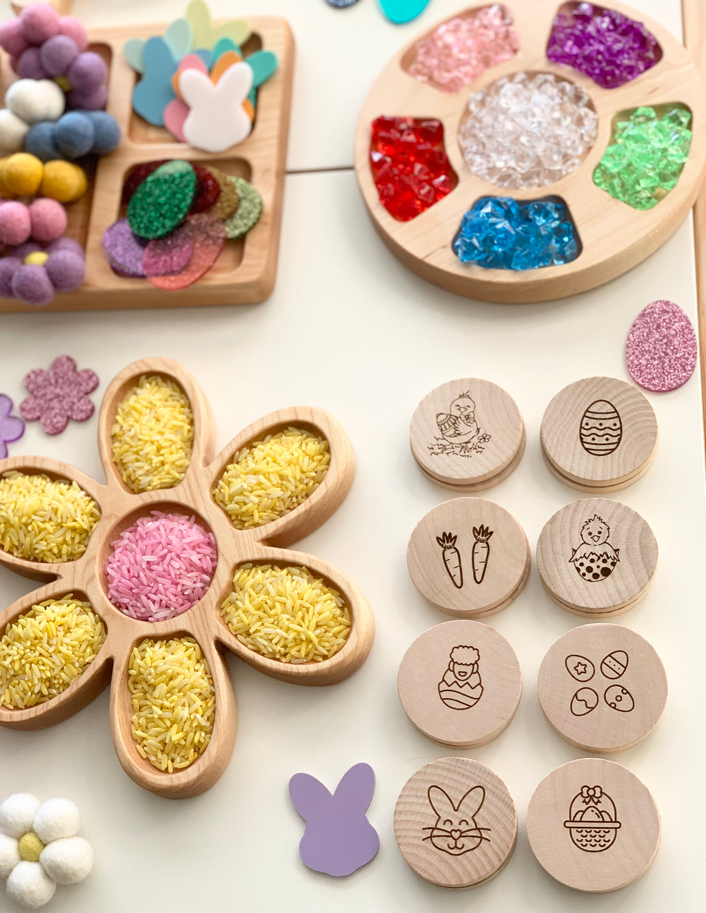 Wooden Easter memory game discs with engraved spring-themed icons arranged next to flower-shaped tray filled with colored rice