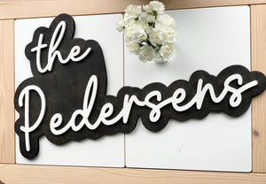 Large custom wooden wedding sign with white cursive letters on dark stained layered wood background with flowers nearby