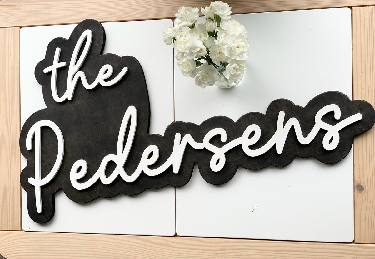 Large custom wooden wedding sign with white cursive letters on dark stained layered wood background with flowers nearby