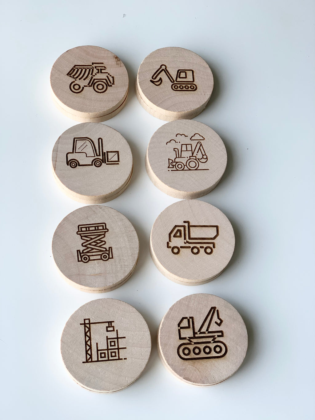 Round wooden memory game discs with engraved construction vehicles and equipment illustrations on natural wood surface
