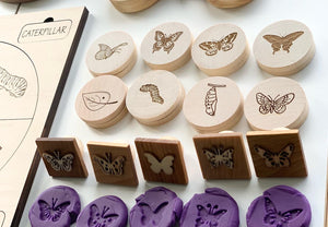 Round natural wooden discs and square wooden tiles engraved with butterfly life cycle stages and butterfly stamps on white surface