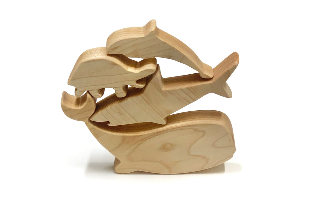 Natural wooden toy figurines of stacked marine animals including whale, dolphin, and crab on white background