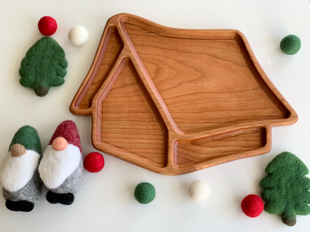 Wooden whimsical house-shaped sensory tray with smooth edges surrounded by felt gnome and tree decorations on white surface