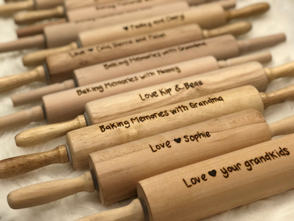 Personalized wooden rolling pins with custom wood burned messages arranged in rows on neutral background