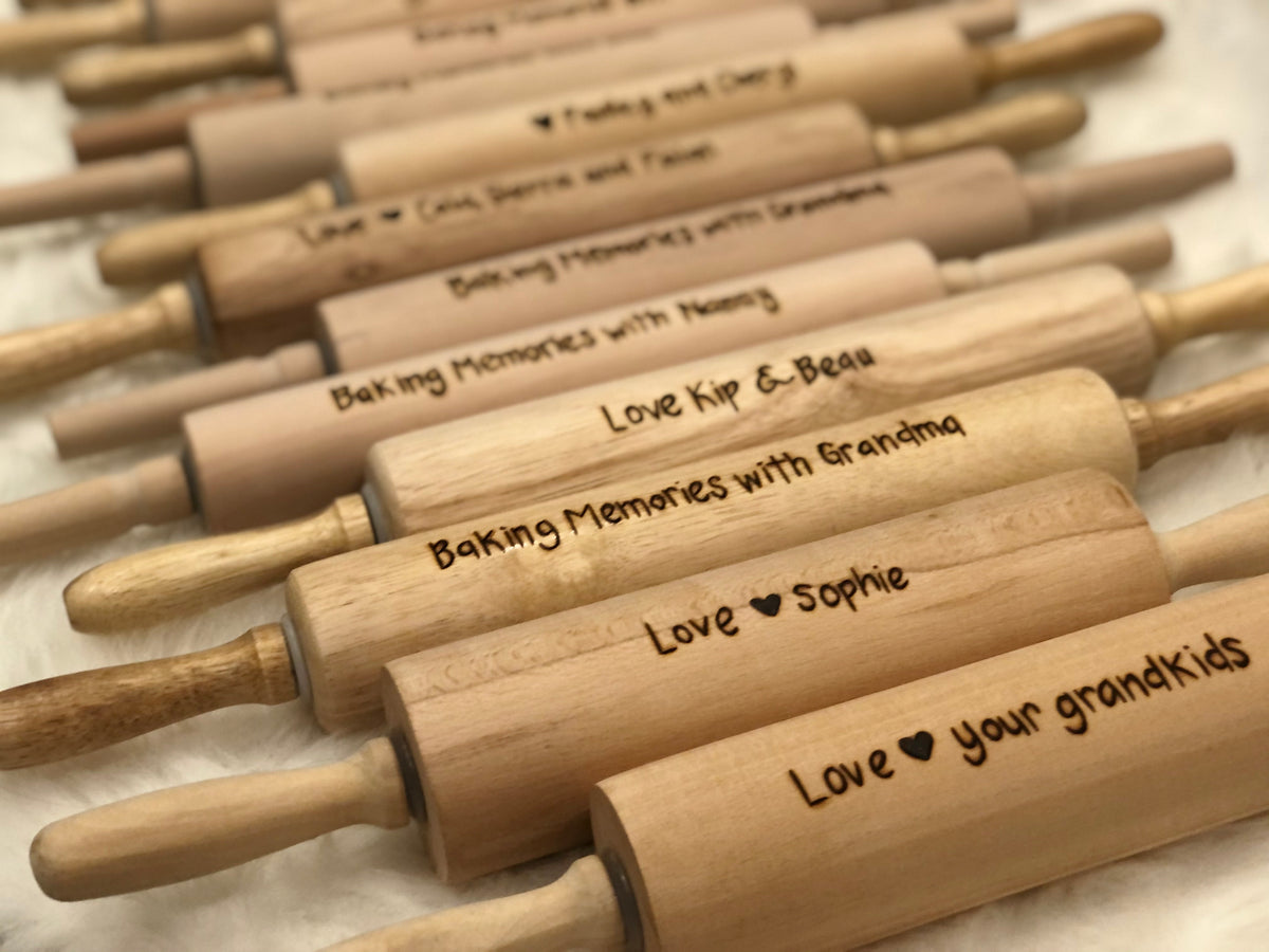 Personalized wooden rolling pins with custom wood burned messages arranged in rows on neutral background