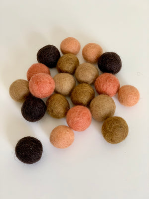 Assortment of tangerine, brown, and beige felt balls scattered on a white surface