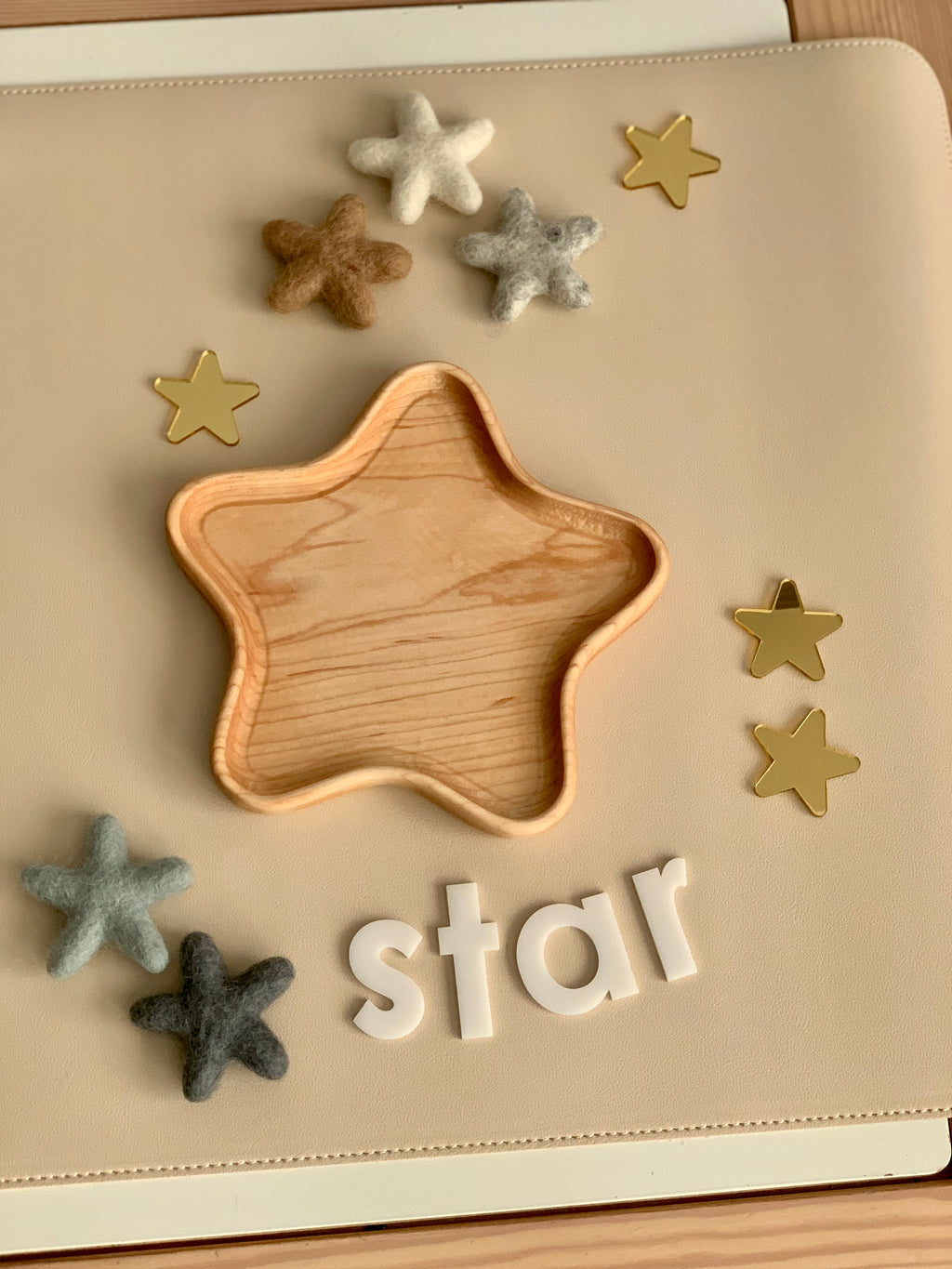 Wooden star-shaped tray surrounded by neutral felt stars and gold star confetti on beige surface with white letters spelling star
