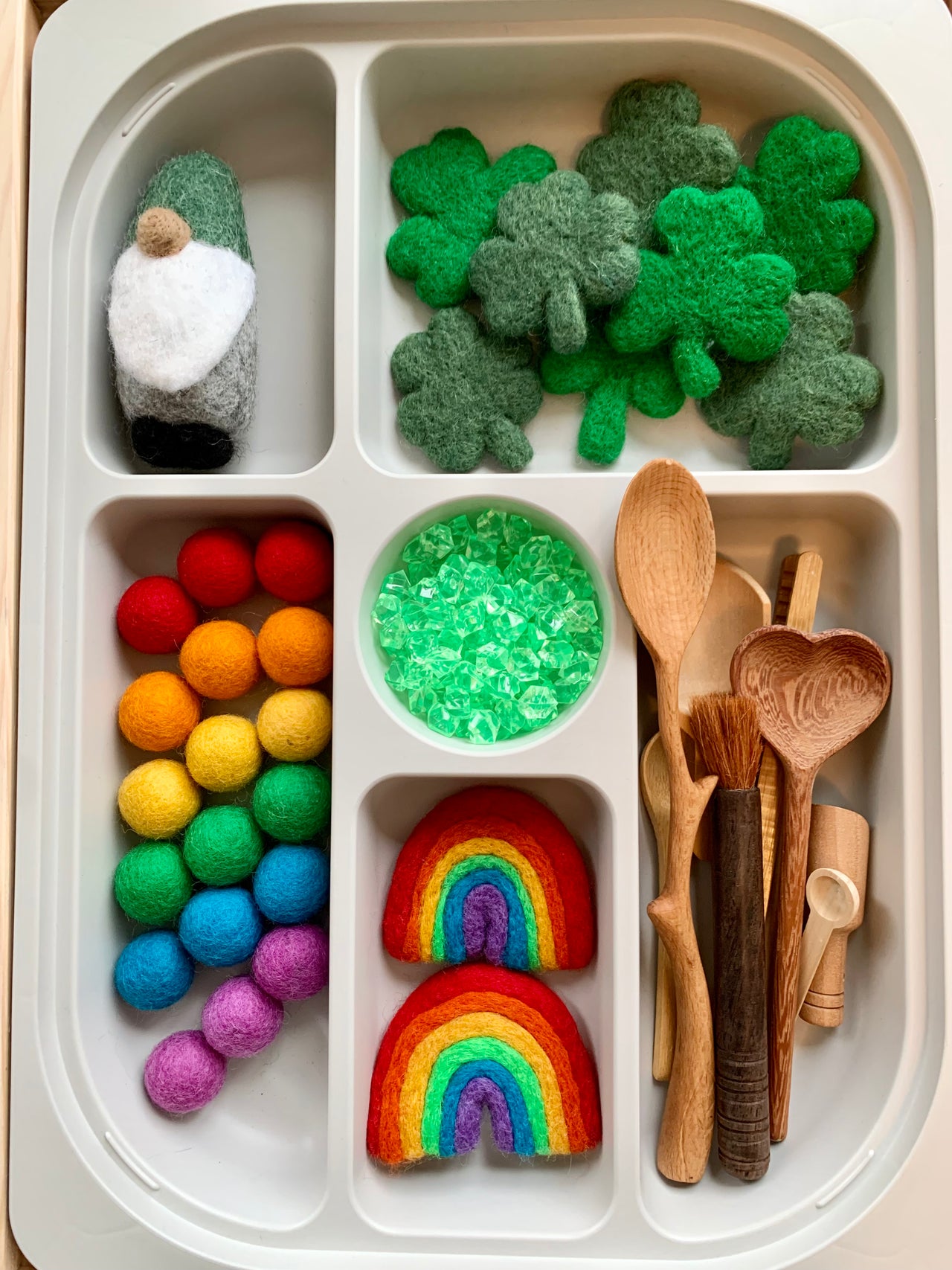 White tray with felt shamrocks, colorful felt balls, wooden spoons, green crystals, rainbow felt pieces, and small felt gnome figure