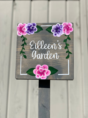 Small square wooden garden sign with white cursive text and hand-painted pink and purple floral designs on dark wood background