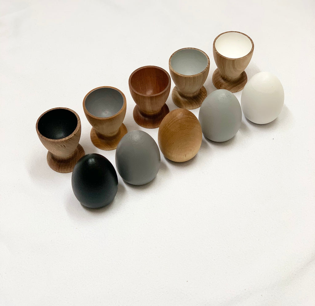 Natural wooden eggs and matching cups in neutral colors for Montessori-inspired educational play and color sorting.