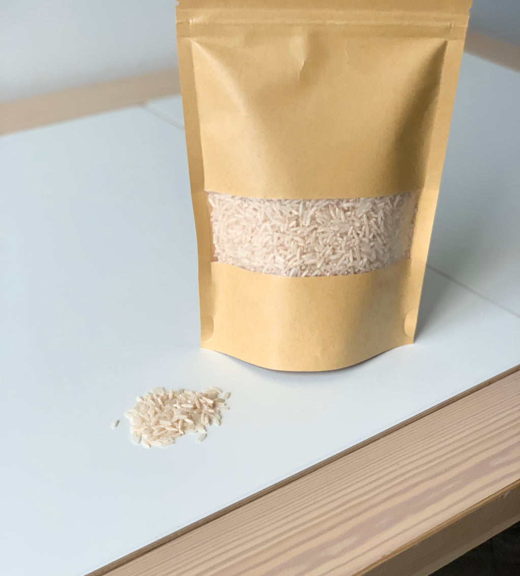 Brown kraft resealable pouch filled with pale pink sensory filler rice spilling onto white table surface