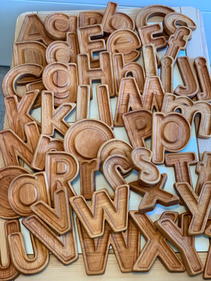 Natural wooden letter sensory trays with carved uppercase and lowercase alphabet letters stacked on light wood surface