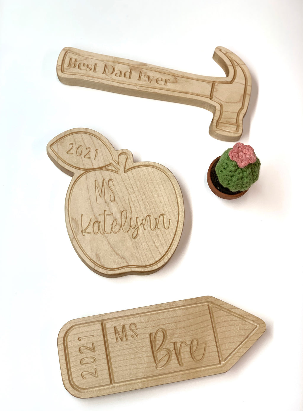 Set of three natural wooden engraved plaques shaped like a hammer, apple, and pencil with personalized names and dates on white background