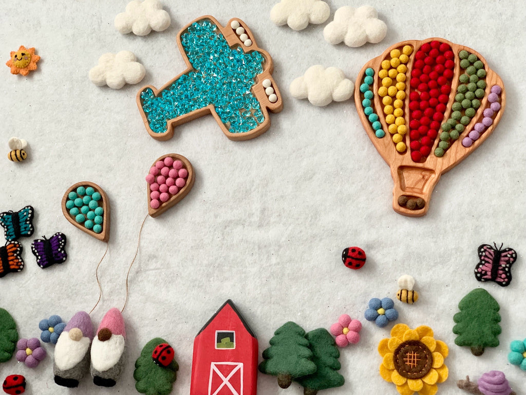 Wooden hot air balloon and airplane sensory trays with felt balloons, flowers, animals, and a barn on white wool background
