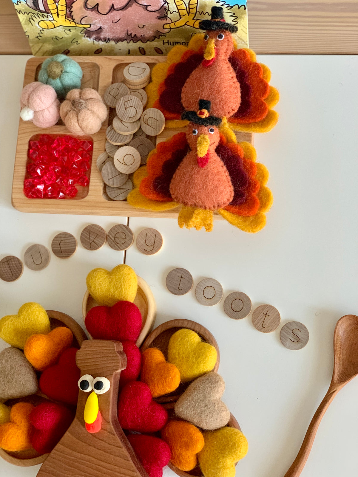 Two handmade felt turkeys with autumn-colored feathers and little black pilgrim hats on white surface with wooden tokens and felt pumpkins