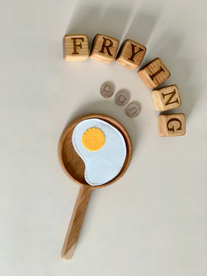 Wooden frying pan sensory tray with felt fried egg and wooden letter blocks spelling fry and ing on white surface