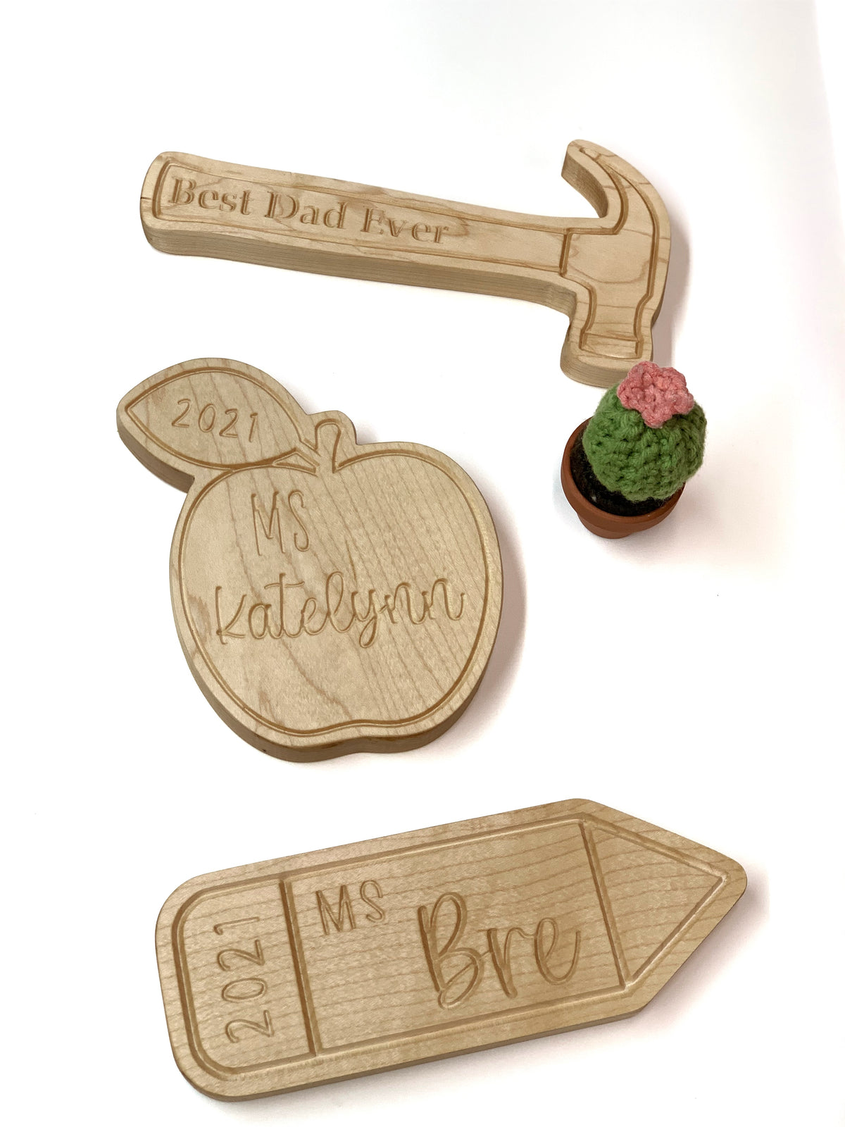Three personalized engraved wooden plaques shaped like a hammer, apple, and pencil with names and dates on white background