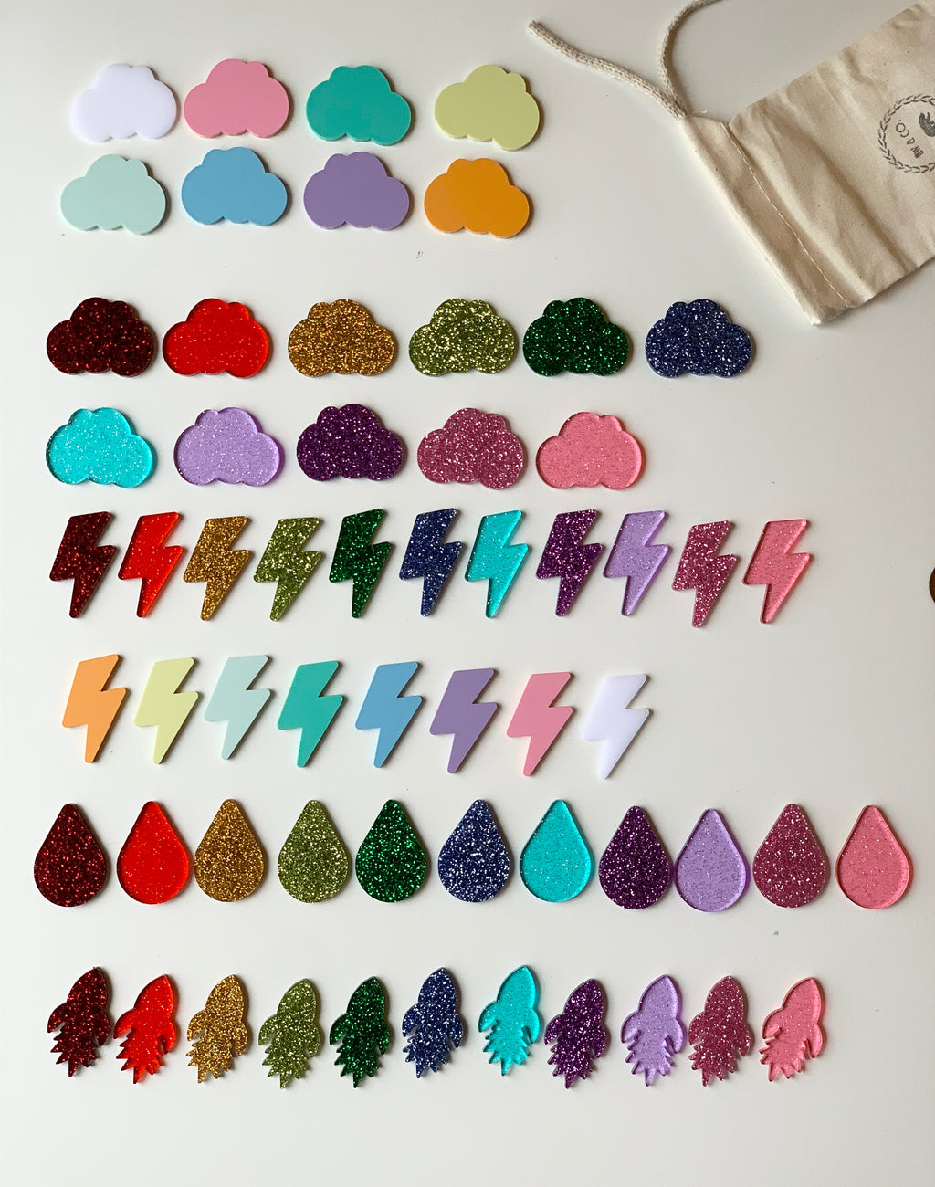 Assorted laser cut acrylic shapes including clouds, lightning bolts, rain drops, and rockets in various colors on white surface