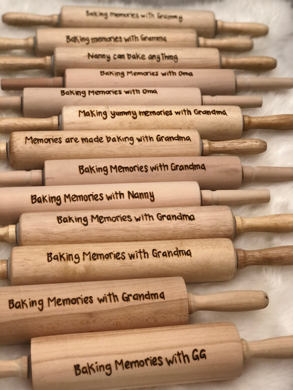 Collection of personalized wooden rolling pins with custom engraved baking messages and names on light wood surface