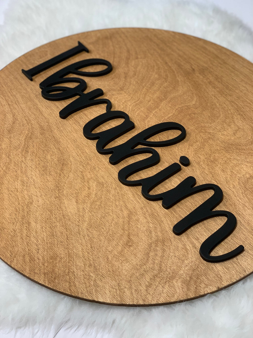 Round wooden nursery sign with smooth finish and raised black cursive personalized name Ibrahim
