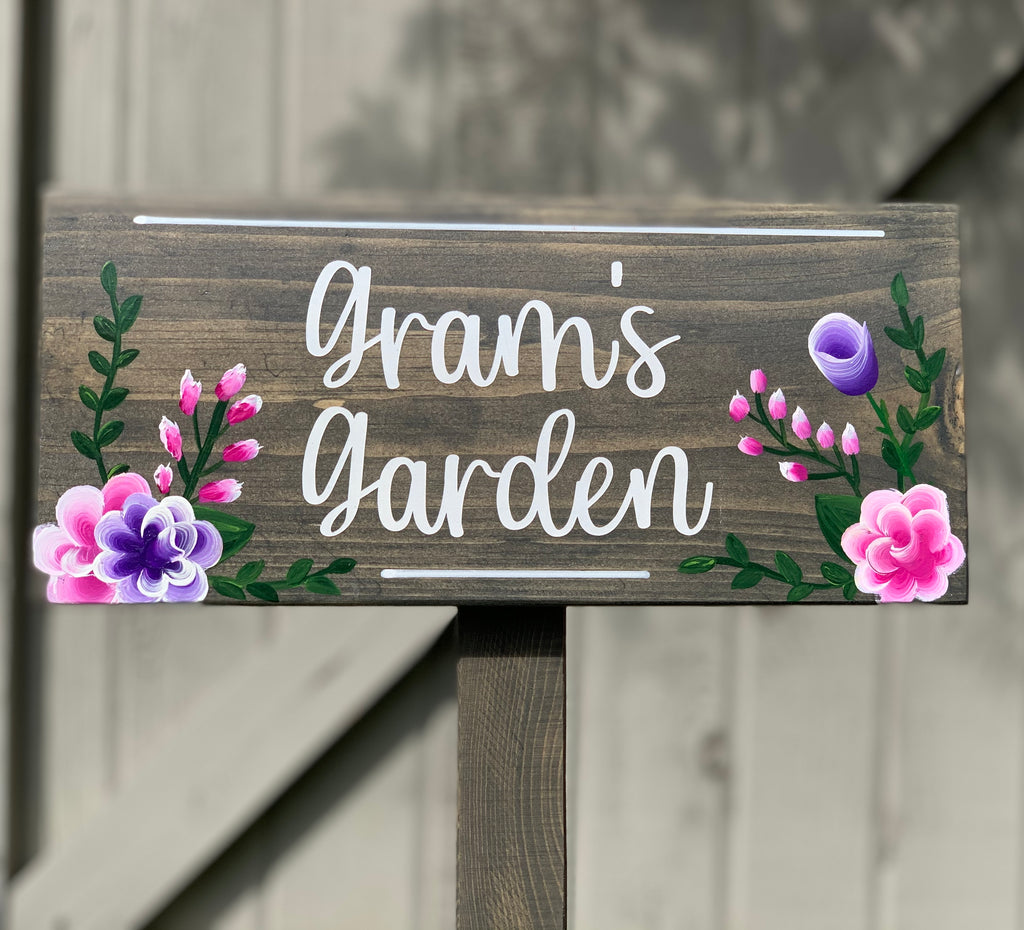 Large custom wooden garden sign with white cursive letters and pink and purple floral illustrations on stained wood background