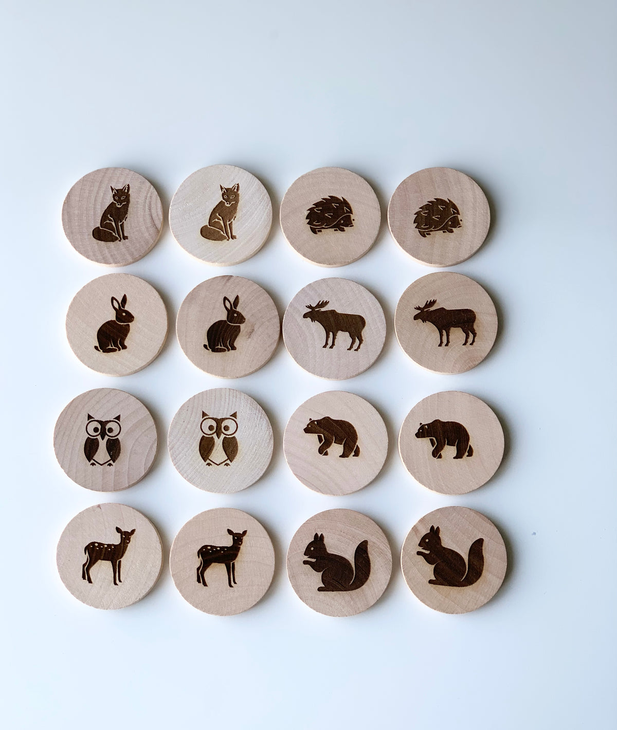 Natural wooden memory game discs with engraved woodland animal pairs on white background arranged in rows