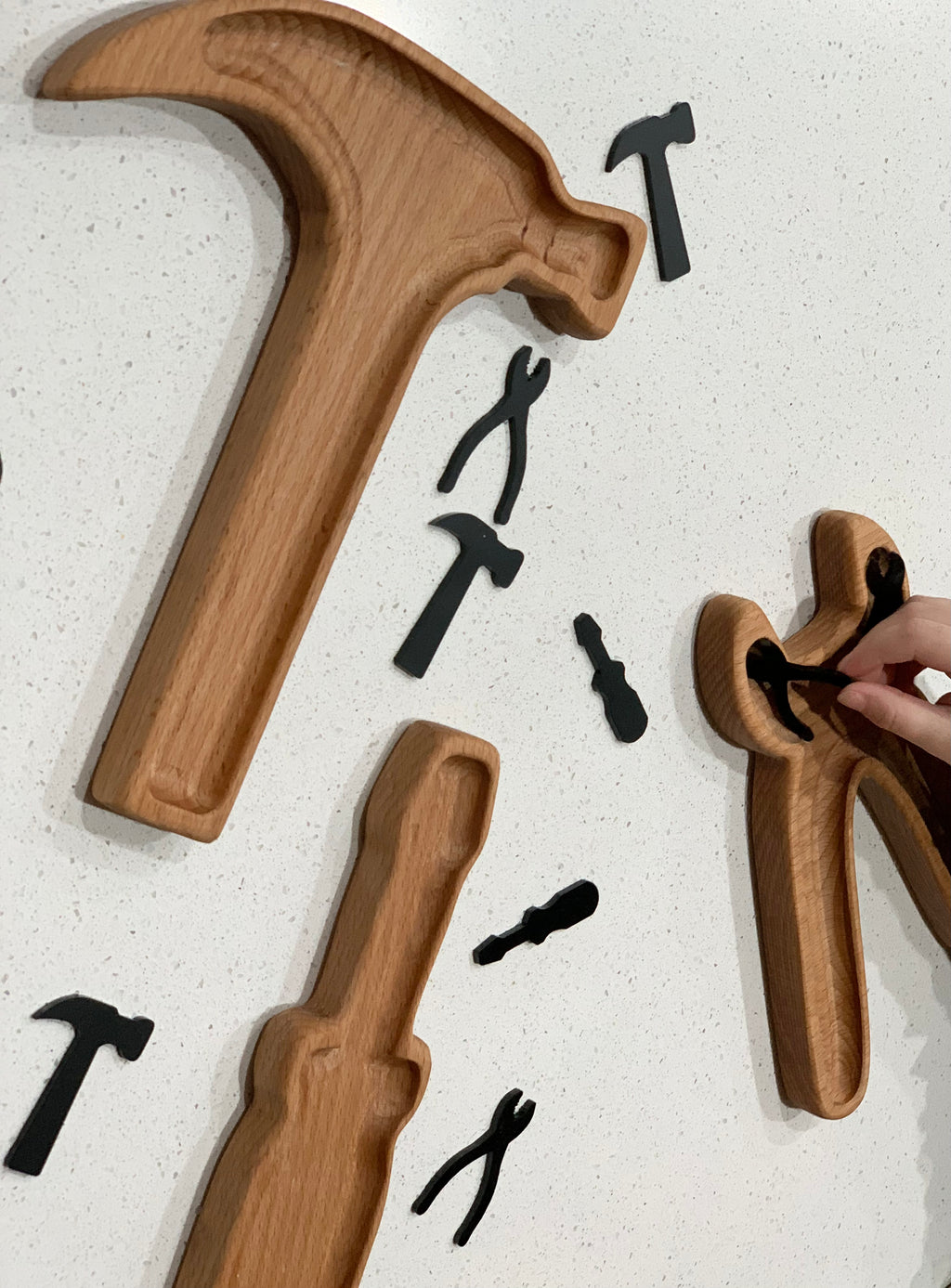 Wooden tool-shaped sensory trays including hammer, screwdriver, and pliers with small black tool figures on white surface