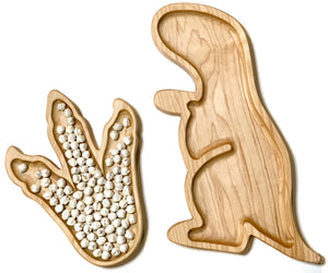 Natural wooden sensory trays shaped like a T-Rex dinosaur and a dinosaur footprint filled with white beads on white background