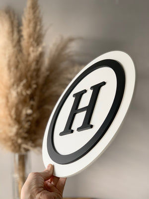 Round 3D monogram sign with black letter H and outline on white layered MDF background held by hand