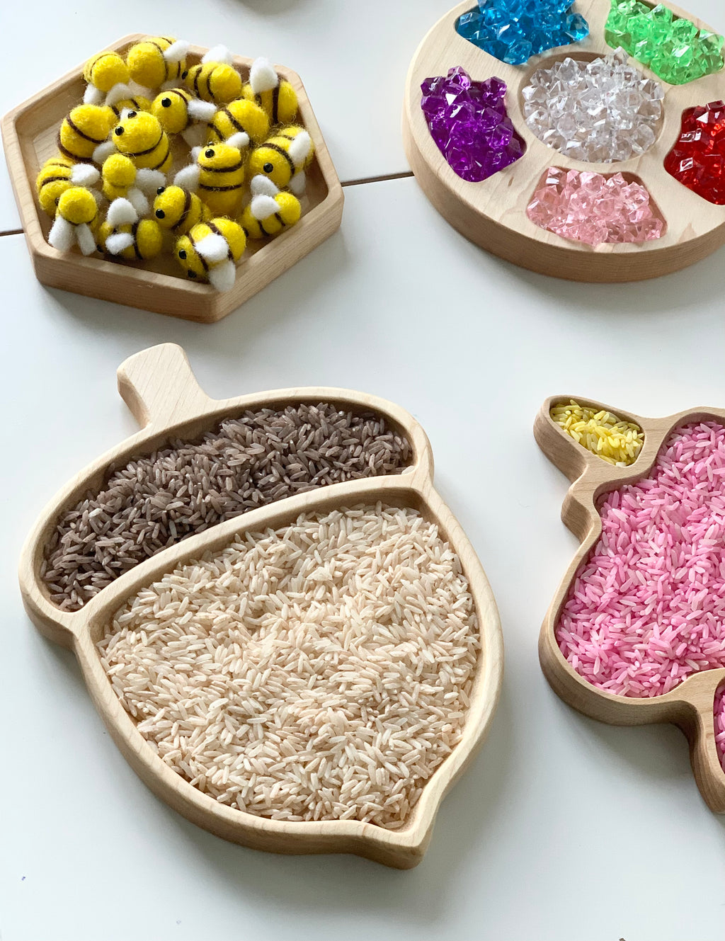 Natural wooden acorn-shaped sensory tray filled with two types of rice on white background with other trays nearby