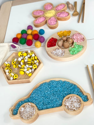 Wooden sensory tray set with colorful rice, felt balls, bees, and translucent gem toppings on white surface