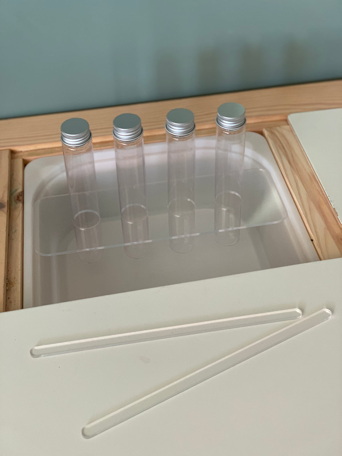Clear acrylic Flisat table top insert holding four plastic test tubes with silver lids on wooden frame
