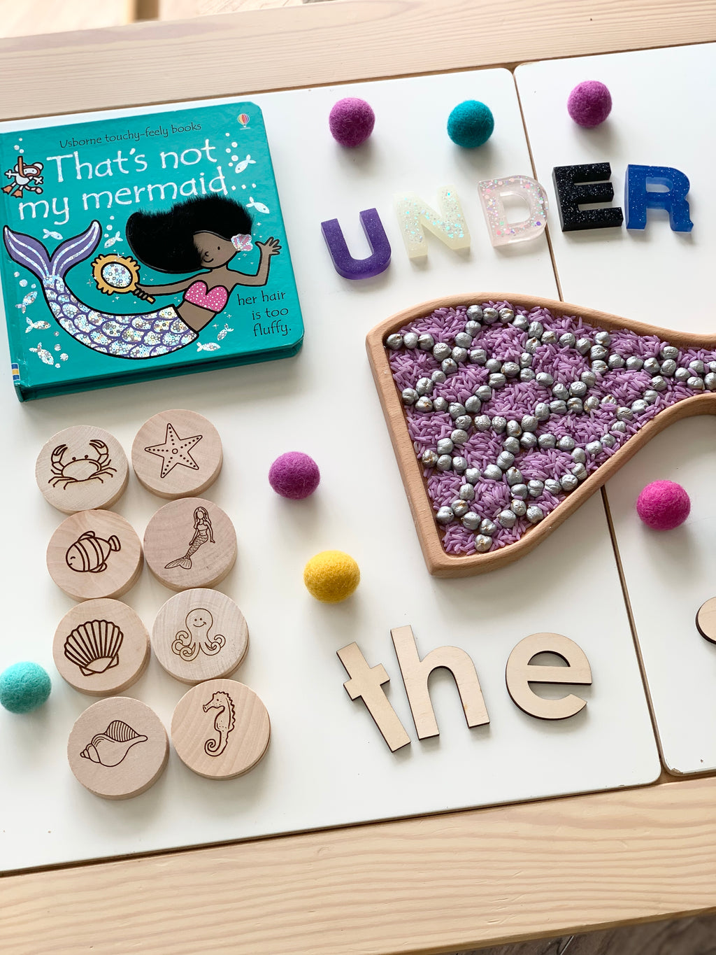 Wooden memory game discs with sea creatures, a children's mermaid book, colorful felt balls, and letters spelling under the sea